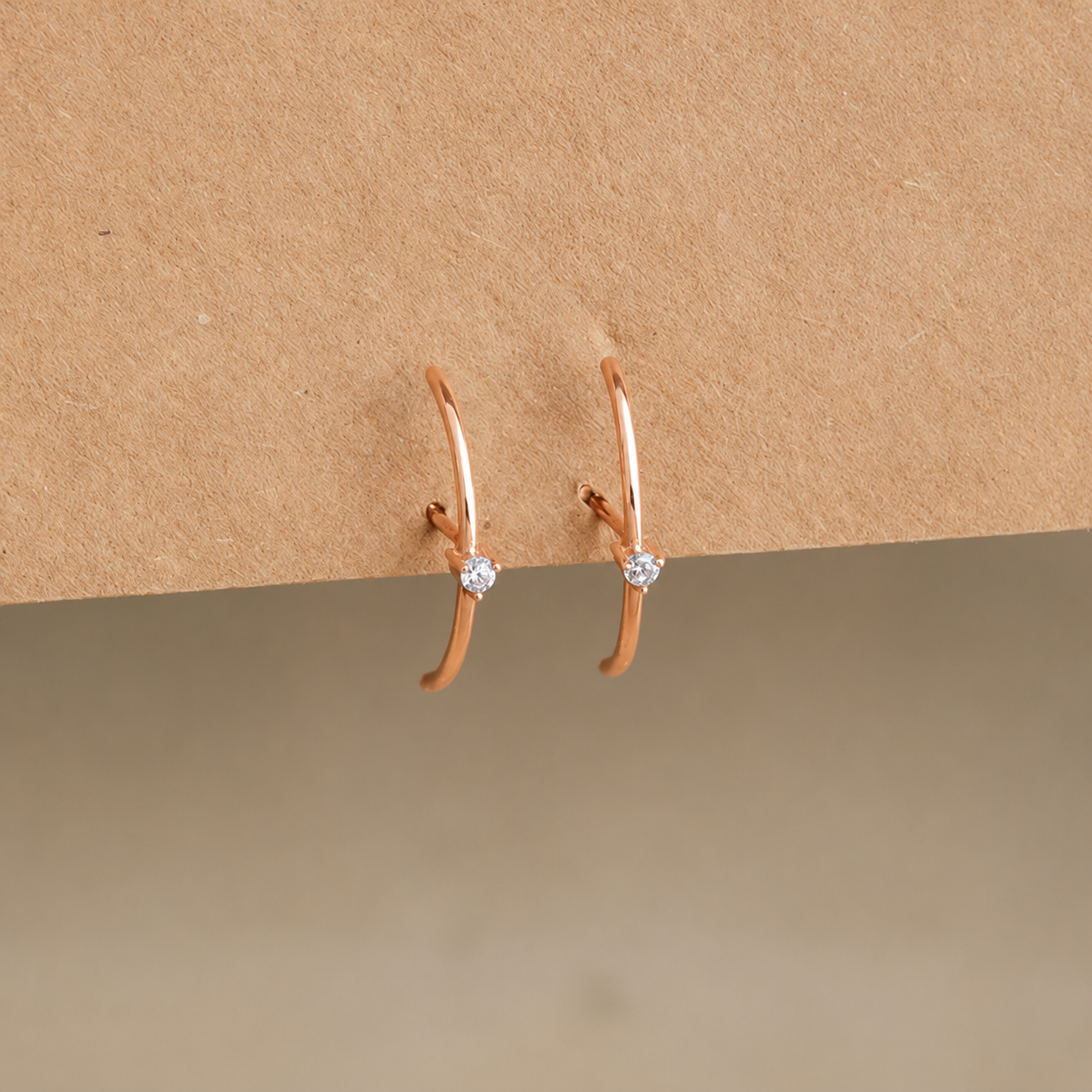 Rose gold hoop earrings with small diamonds on a beige background